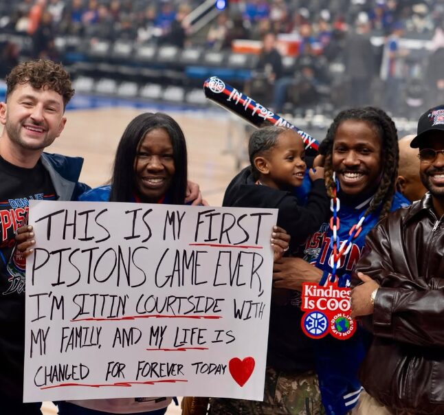 Family courtside at their first Pistons game holding a sign reading their life was changed